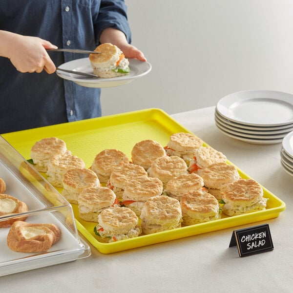 A person holding a Choice yellow bakery display tray with biscuits on it.