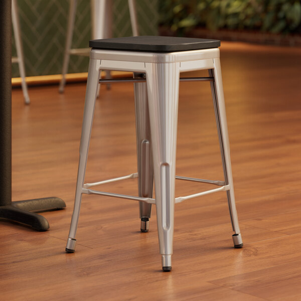 A Lancaster Table & Seating metal backless counter height stool with a black wood seat.