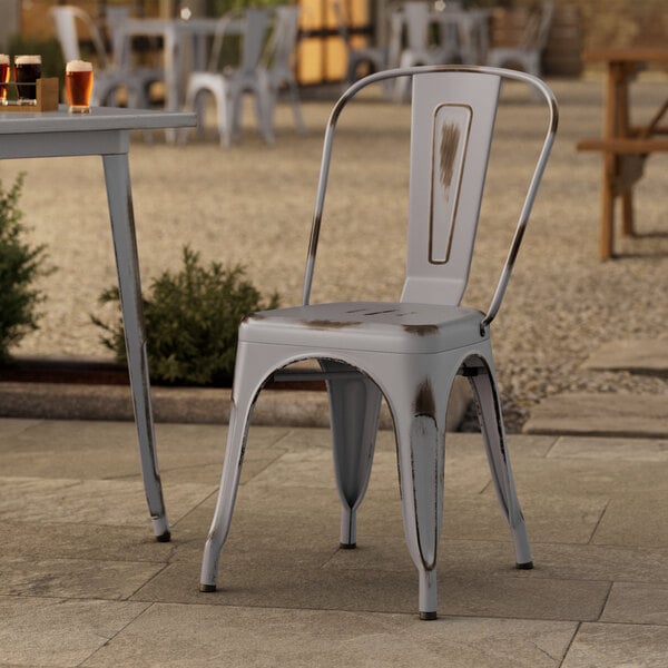 A Lancaster Table & Seating distressed nickel gray metal chair on an outdoor stone patio.