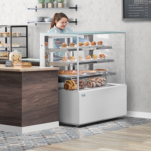 A woman looking at a white Avantco dry bakery display case filled with pastries.