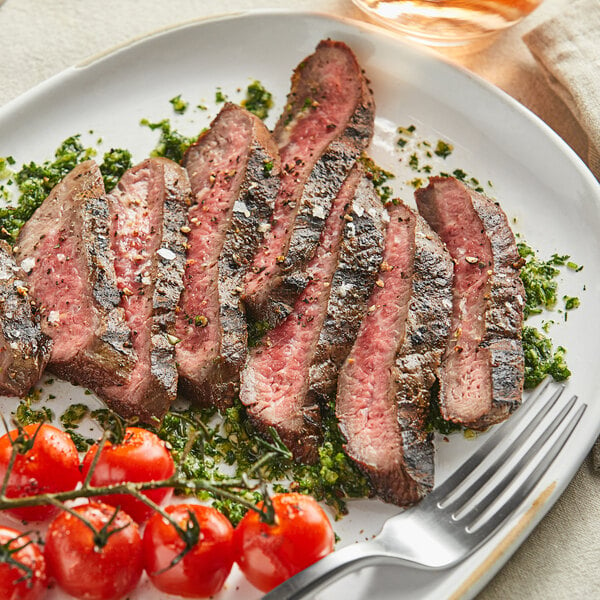 Bavette steak on a white plate with pesto sauce and roasted cherry tomatoes
