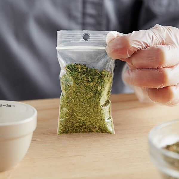 A hand holding a Choice clear plastic bag of green herbs.