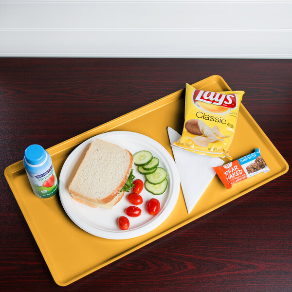 A Cambro mustard dietary tray with a sandwich, chips, and a drink on it.