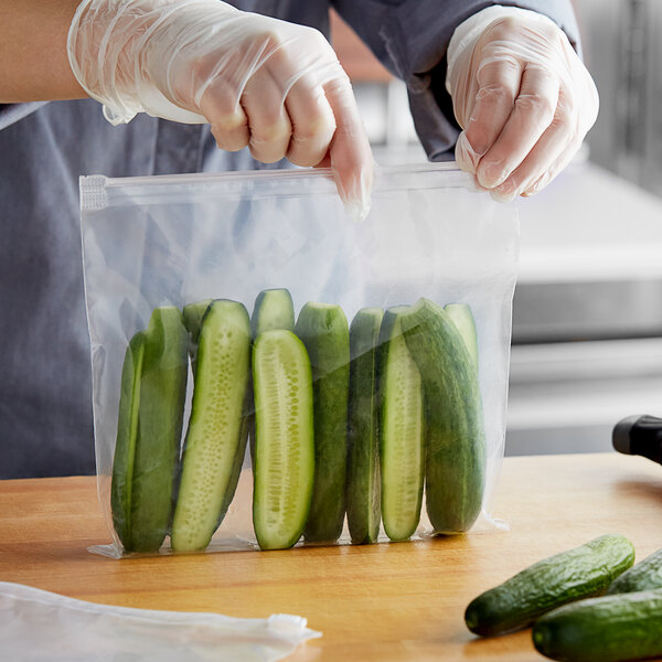 A person in gloves holding a Choice clear plastic slider top bag of cucumbers.