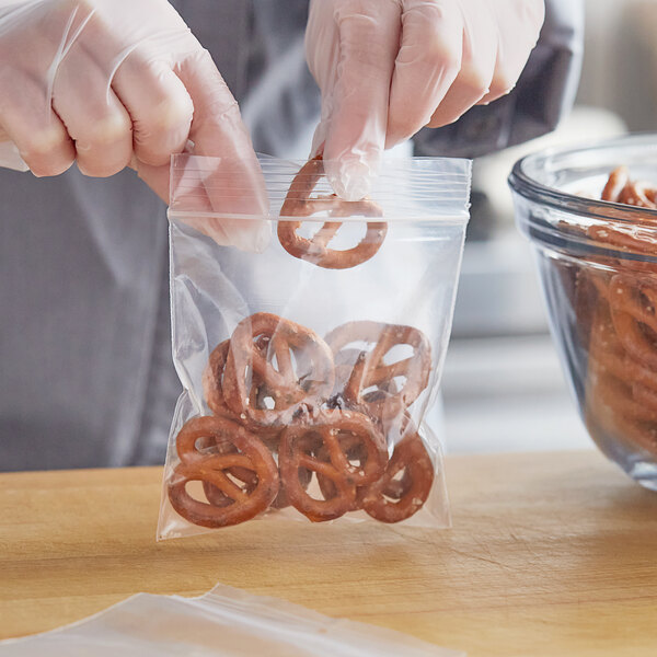 A person in gloves holding a Choice polypropylene zip top bag of pretzels.