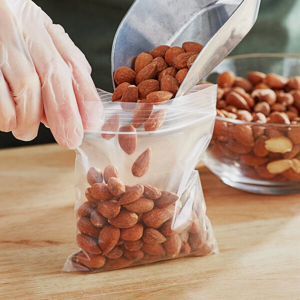 A gloved hand pouring almonds into a Choice 4" x 4" clear zip top bag.