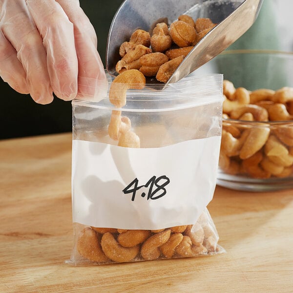 A person wearing gloves pouring nuts into a Choice 4" x 4" clear plastic bag.