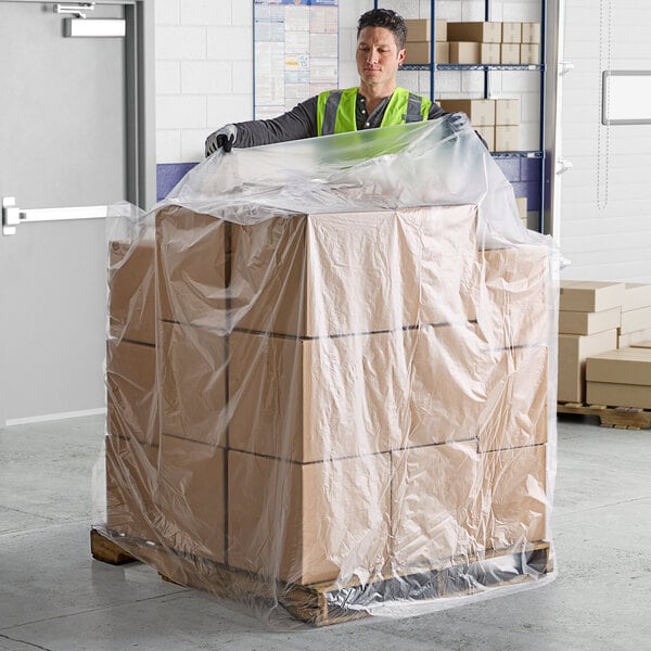 A man in a yellow safety vest and gloves holding a large box of Lavex gusseted pallet covers.