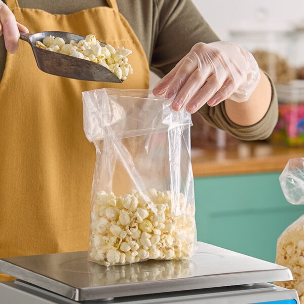 A hand using a scoop to pour popcorn into a Choice clear polypropylene layflat bag.