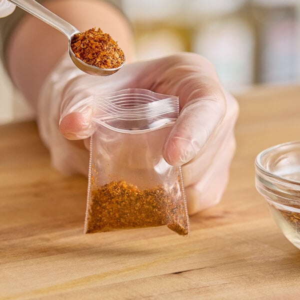 A hand holding a Choice 2" x 2" clear LDPE zip top bag of spices with a spoon.