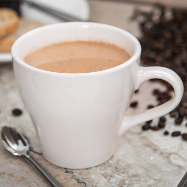 A close-up of a Tuxton Europa white coffee mug with brown liquid and a spoon.