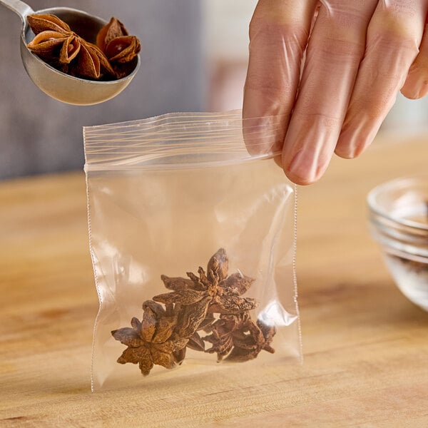 A hand using a spoon to add star anise to a Choice clear zip top bag.