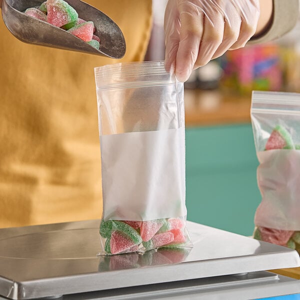 A hand in a plastic glove holding a Choice clear plastic bag with white block full of candy.