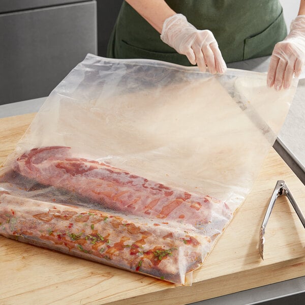 A person wearing gloves slides a Choice clear LDPE bag over a piece of meat.