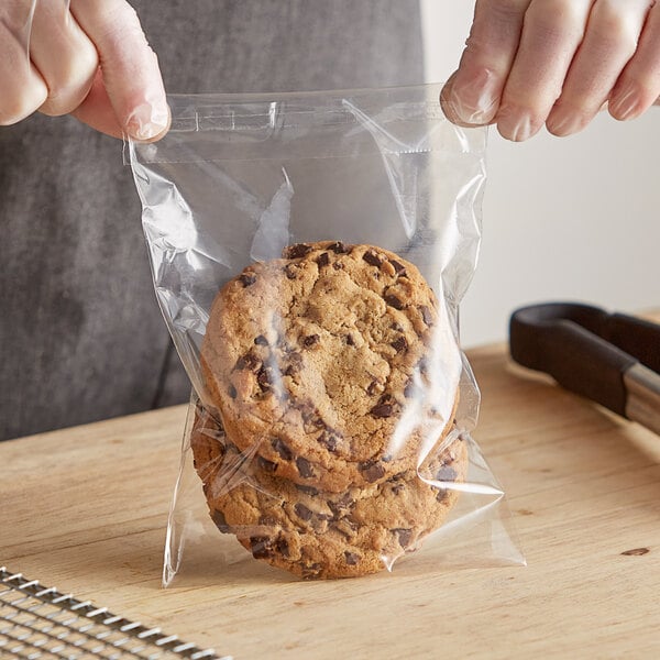 A hand holding a Choice 1.6 mil polypropylene resealable bag of chocolate chip cookies.