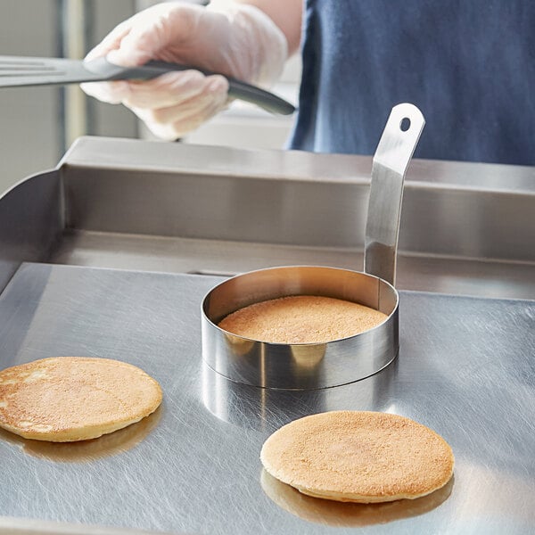 A person using the Choice 4" Stainless Steel Egg Ring to cook a pancake on a pan.
