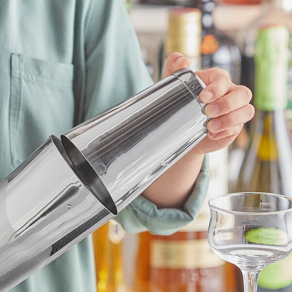 A person holding an Acopa stainless steel cocktail shaker on a counter in a cocktail bar.