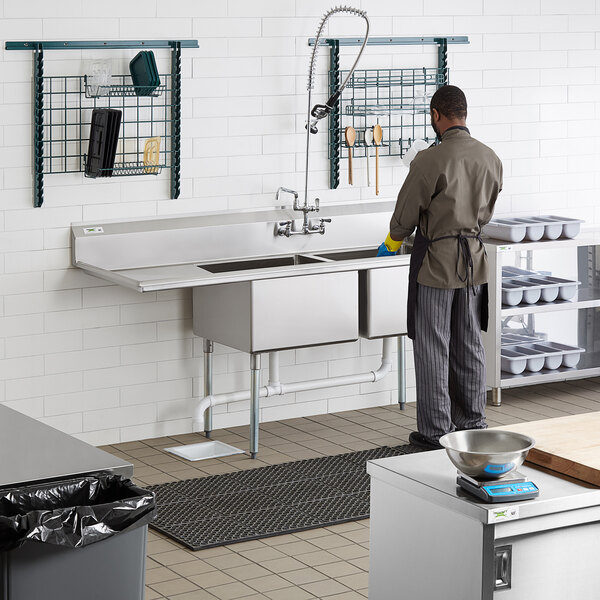 A man standing in a commercial kitchen with a Regency two compartment sink with a left drainboard.