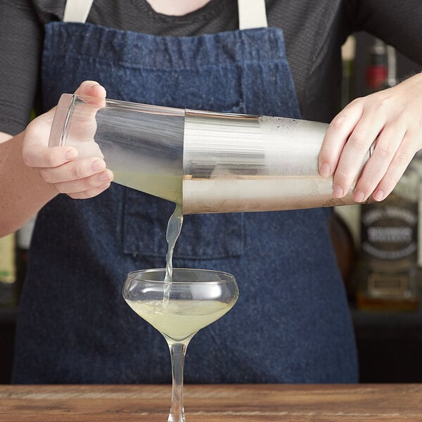 A person using an Acopa stainless steel cocktail shaker to pour a drink.