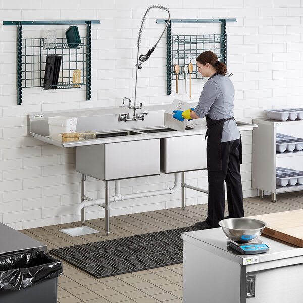 A woman washing dishes in a Regency two compartment commercial sink.