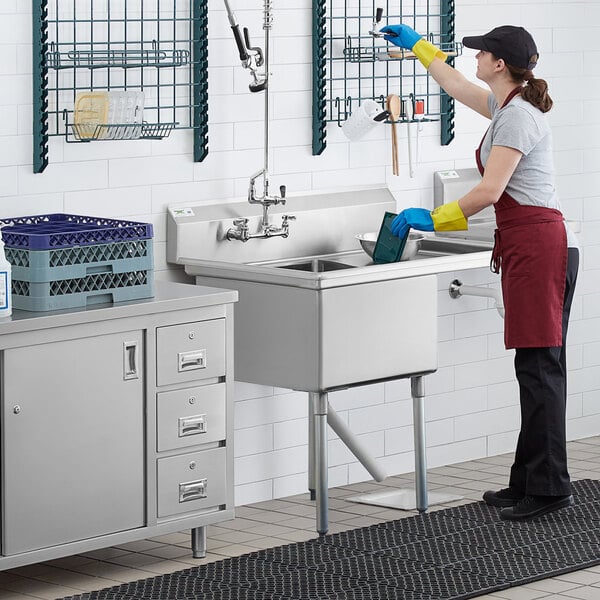 A woman wearing gloves cleaning a Regency stainless steel commercial sink.