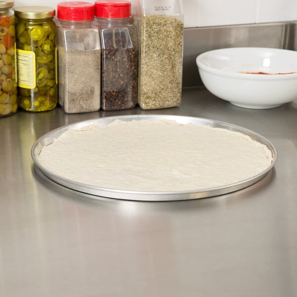 A pizza on a metal pan with spices on the counter.
