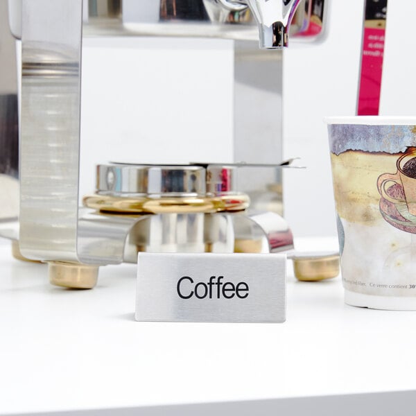 A stainless steel double sided table tent sign that says "Coffee" on a table with a coffee cup.