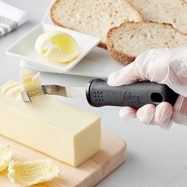 A person using a Choice butter curler with a black handle to cut butter on a cutting board.