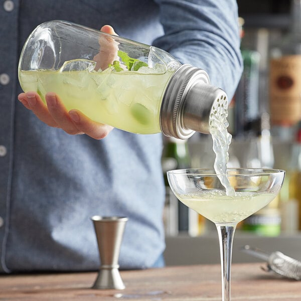 A man using an Acopa Glass Mason Jar Cocktail Shaker to pour a drink into a glass.