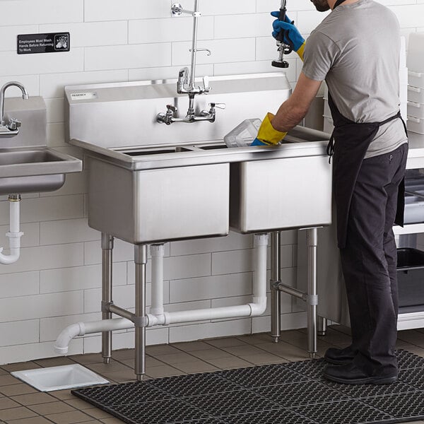 A man in an apron and gloves washing a Regency two compartment commercial sink.