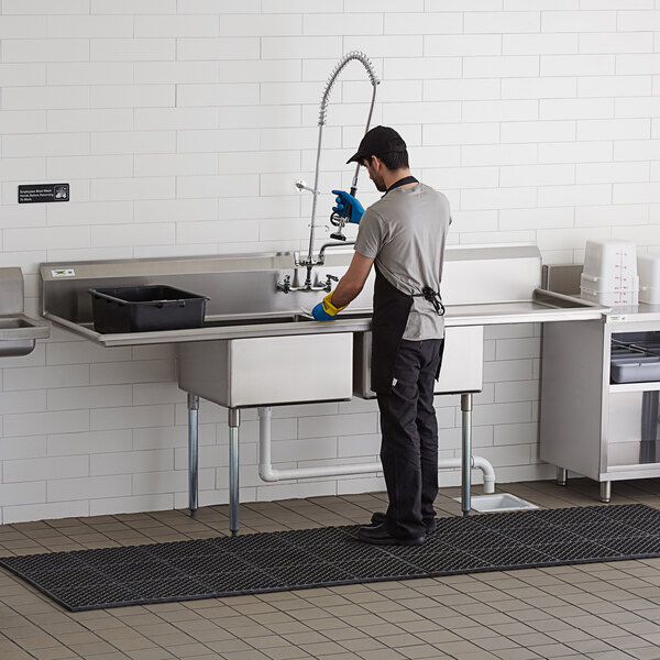 A man washing dishes in a Regency two compartment commercial sink.