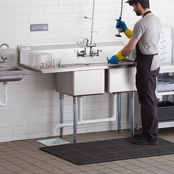 A man wearing gloves washing a Regency stainless steel two compartment sink.