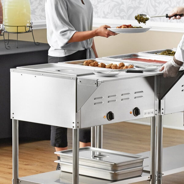 A woman serving food in a commercial kitchen using an Avantco mobile electric steam table.