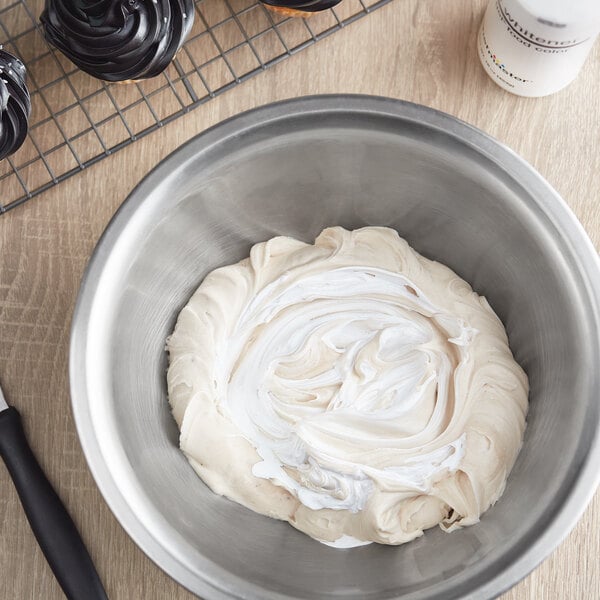 A bowl of white frosting with cupcakes on a counter with a white bottle of Chefmaster Liqua-Gel Food Coloring Whitener on the side.