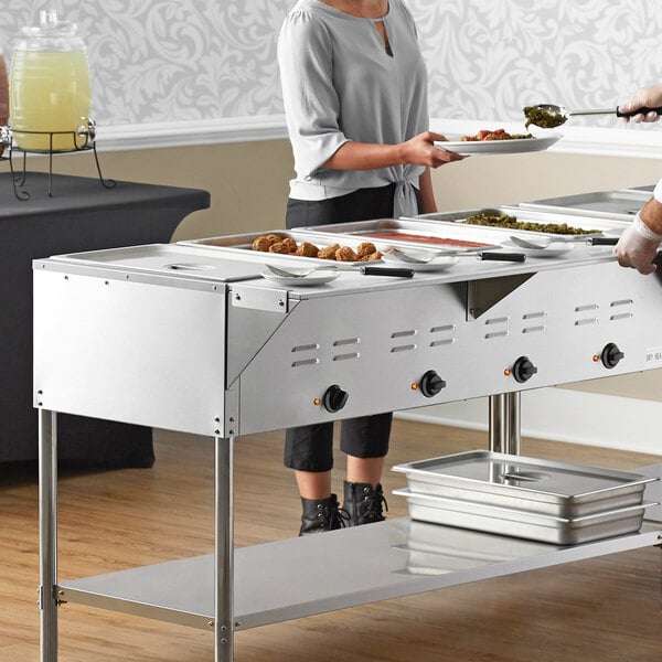 A woman serving food from an Avantco mobile electric steam table to a man and woman at an outdoor catering event.