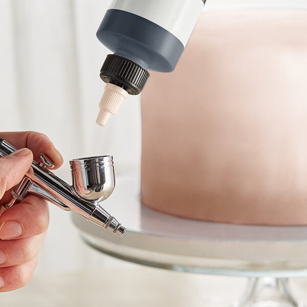 a person holding a spray gun over a cake