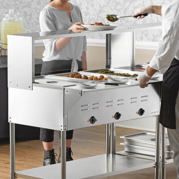 A man and woman in uniforms using an Avantco electric steam table on a counter.