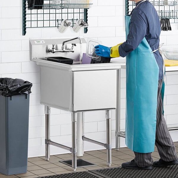 A man in a blue apron and gloves using a Regency stainless steel commercial sink.