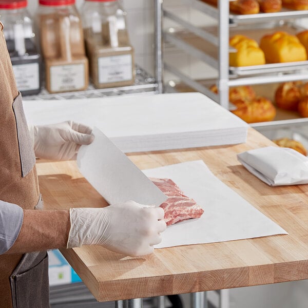 A person wrapping meat in white paper on a table.