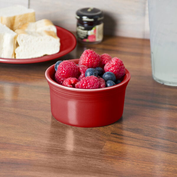 A Fiesta Scarlet China Ramekin filled with raspberries and blueberries on a table.