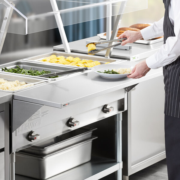 A man using a ServIt solid stainless steel tray slide on a steam table.