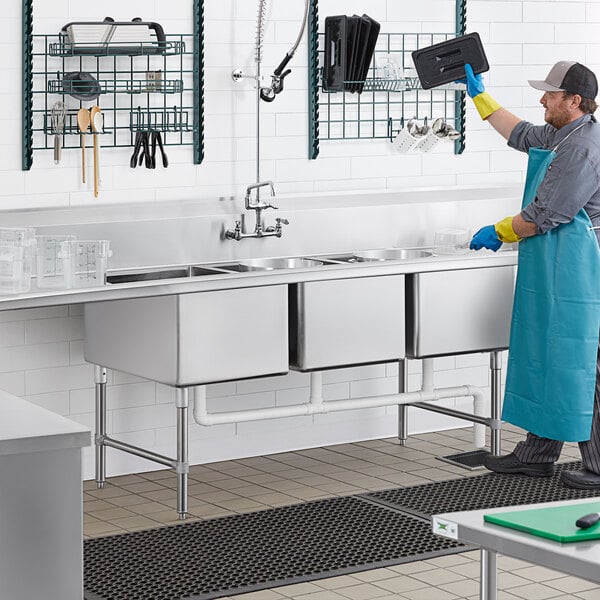 A man in a blue uniform and apron washing dishes in a commercial kitchen.