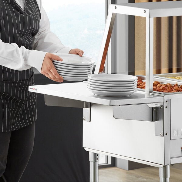A person using a ServIt solid end tray slide on a steam table to hold plates.