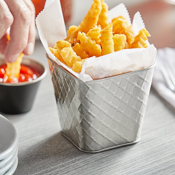 A person dipping a french fries into a Tablecraft stainless steel fry cup.