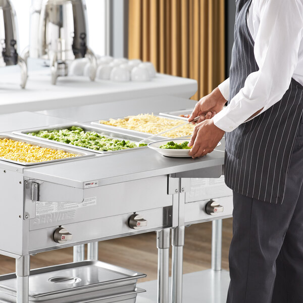A man in a chef's uniform uses a ServIt solid drop down side tray slide on a steam table to prepare food.