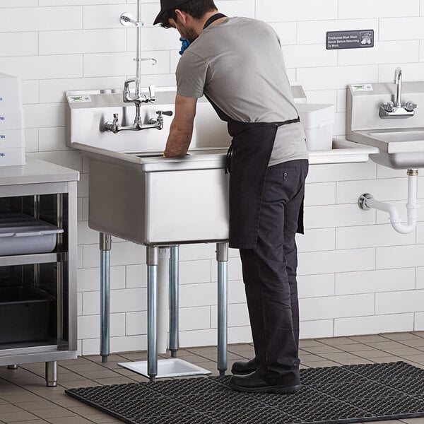 A man standing in a Regency stainless steel commercial sink with a drainboard.