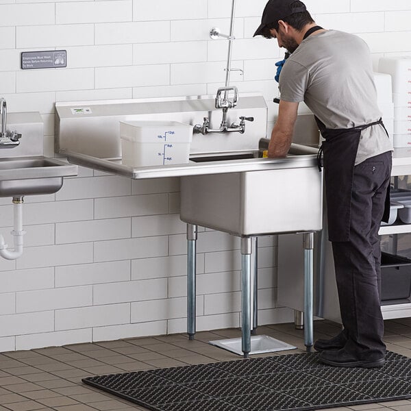 A man washing dishes in a Regency stainless steel commercial sink with a left drainboard in a professional kitchen.