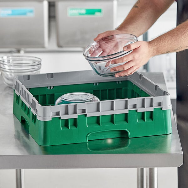 A person putting a glass bowl into a green Cambro dish rack with grey sides.