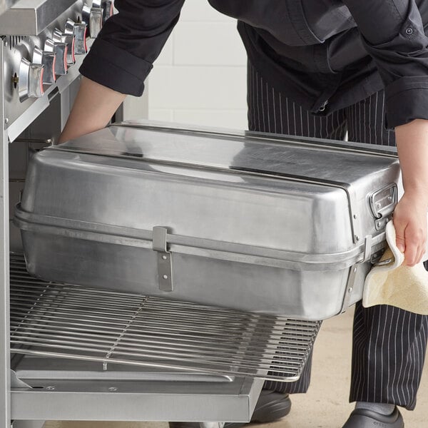 A woman in a chef's uniform using a Choice aluminum double roaster pan to cook on a counter in a professional kitchen.