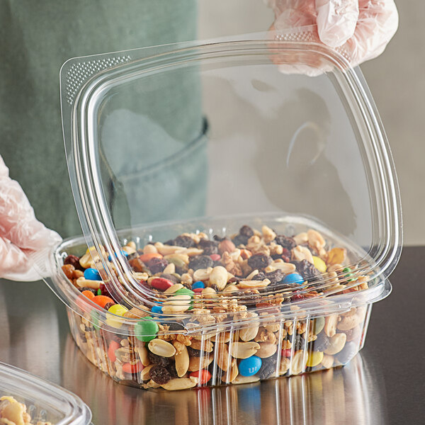 A person holding a Choice clear plastic deli container filled with nuts and candy.